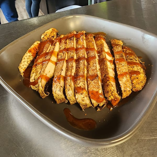Sliced F325 BBQ chicken breast, seasoned and drizzled with barbecue sauce on a dark plate.