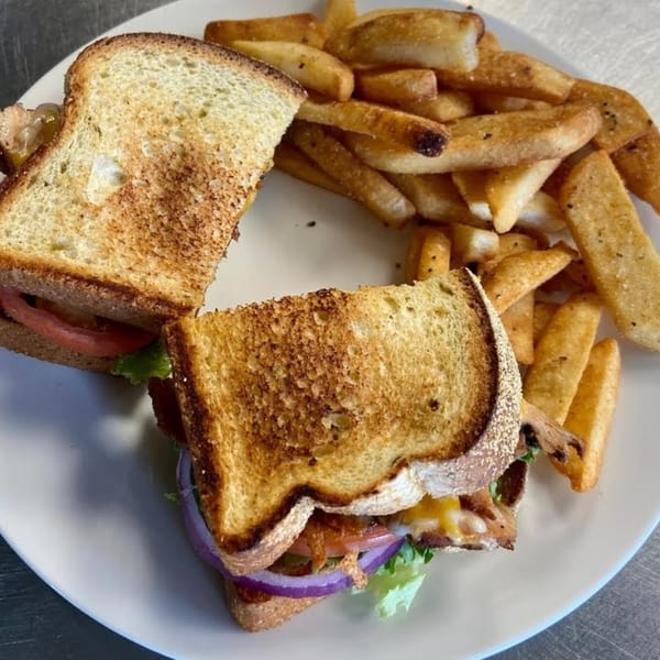 A BBQ sandwich with bacon, lettuce, tomato, and red onion, served with a side of fries.