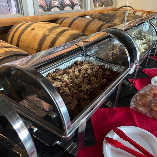 Chafing dishes filled with F325 BBQ pulled pork and other food, with whiskey barrels in the background.